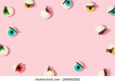 Creative pattern or frame made with eyeball figurines with eyelashes on pastel pink background. Halloween minimal creative concept. Rainbow colored eyes. Modern fashion aesthetic idea.