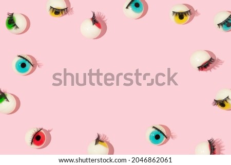 Creative pattern or frame made with eyeball figurines with eyelashes on pastel pink background. Halloween minimal creative concept. Rainbow colored eyes. Modern fashion aesthetic idea.