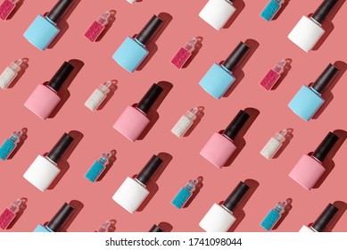 Creative pattern of nail polish bottles in pink, blue and white on a pink background and beads. The concept of summer mood, bright colors and delicious sweet and fashionable manicure and pedicure