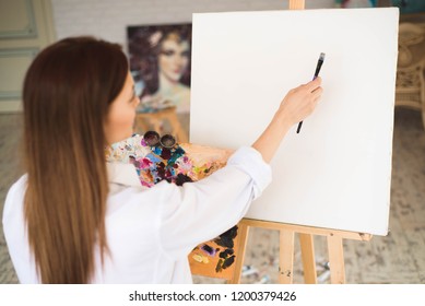 Creative pensive painter paints a colorful picture. Closeup of painting process in art workshop Creative positive woman painter paints in her studio. - Shutterstock ID 1200379426