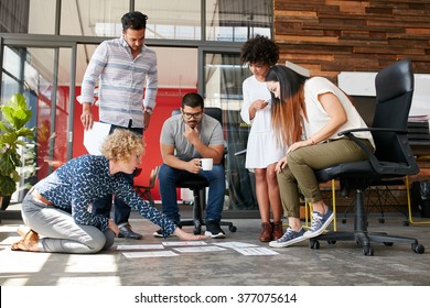 Creative people looking at project plan laid out on floor. Mixed race business associates discussing new project plan in modern office. - Powered by Shutterstock