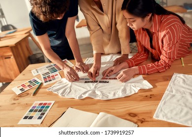 Creative People Trying On Stickers With Text, While Discussing Logo And Design Of T-shirt. Young Man And Women Working Together At Custom T-shirt, Clothing Printing Company. Cropped Shot