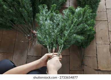 Creative person hand assembles an artificial pine branch for Christmas tree. festive DIY project involves crafting decoration on stone floor for holiday season