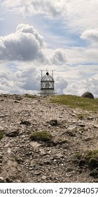 Creative perspective of the iconic Estaca de Bares Lighthouse at the northern tip of the Iberian Peninsula. The frame highlights the unique crisscrossed glass enclosure of the beacon chamber sitting atop a green, rocky pasture under a bright, overcast sky.