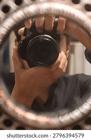 Creative perspective of a man capturing a self-portrait with a professional camera using a round vintage-style mirror frame.
