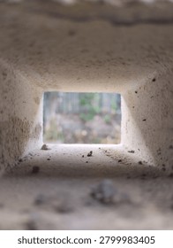 Creative perspective view through a rectangular hollow concrete block, showcasing depth, texture, and selective focus. The rough interior surface and geometric frame create an abstract architectural composition with natural light and a blurred outdoor background.