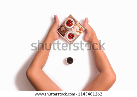 Creative photo of box with cakes between female feets on white background. Top view