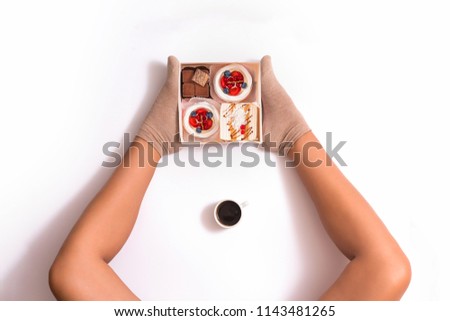 Creative photo of box with cakes between female feets on white background. Top view