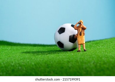 Creative Photo With A Soccer Ball On The Lawn And A Tourist Photographer. Macro Shooting. Sports Background. Miniature People.