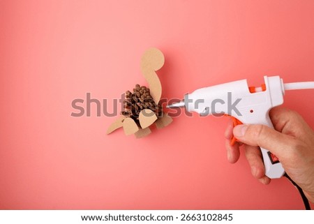 Creative pinecone dinosaur craft with glue gun on pink background, ideal for kids education, DIY blogs, eco-friendly brands, toy stores, and preschool marketing.