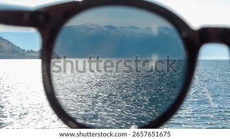A creative point-of-view shot looking through sunglasses at the sparkling Sognefjord in Norway, framing the majestic, snow-capped mountains and emphasizing a clear, protected vision on a sunny day.