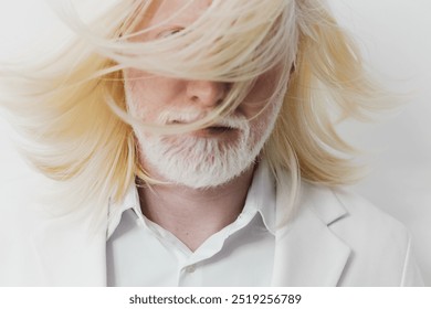 Creative portrait of an androgynous man with long blonde hair and beard, wearing a white suit against a minimalistic white background, conveying a sense of modern elegance and style - Powered by Shutterstock