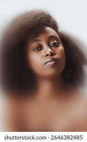Creative portrait. Elegant woman with natural afro hair gazes confidently through softened focus and blurred gradient. Concept of beauty, emotion, strength, identity. Blur effect.