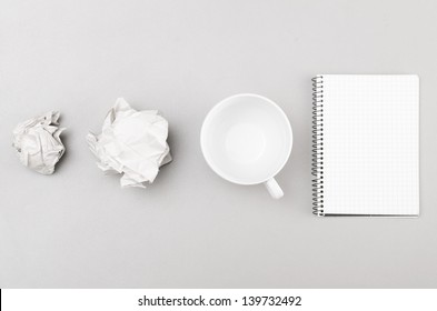 creative process. crumpled wads, notebook and cup on gray