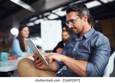 The creative process. Shot of a man sitting at a table in an office using a digital tablet with colleagues working in the background. - Powered by Shutterstock