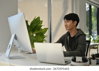 Creative professional editing content working at a desk with a desktop and laptop in a bright, modern office setting.