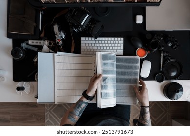 Creative professional photographer examines film negatives on a well-organized, contemporary workspace with various photography equipment around. - Powered by Shutterstock