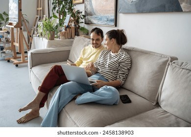 Creative relaxed happy couple sitting on comfortable couch with laptop at home art studio. Smiling woman artist discuss with man collaboration project, rest in craft workshop. Teamwork brainstorming. - Powered by Shutterstock