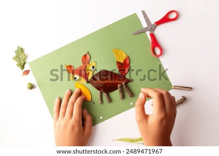 A creative representation of a fox made from various autumn leaves and natural elements on a green background.