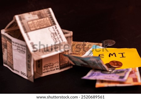 A creative representation of Indian currency notes arranged to form a house, alongside a handwritten yellow note labeled "EMI," symbolizing home loans, mortgages, and financial planning.