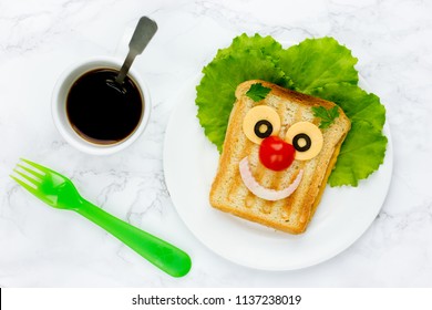 Creative Sandwich For Kids Healthy And Funny Breakfast. Clown Face Fried Sandwich With Green Salad, Cheese, Tomato And Ham On White Plate Top View