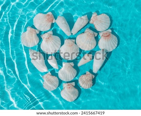 Creative scene of love heart symbol made with sea shells in water on bright blue background. Minimal summer concept. Original background image with a play of light and shadow. Summertime love idea.