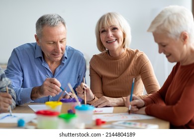 Creative senior people enjoying painting class at sanatorium, group of elderly men and women sitting at table, holding painting brushes, chatting and smiling while having art-therapy - Powered by Shutterstock