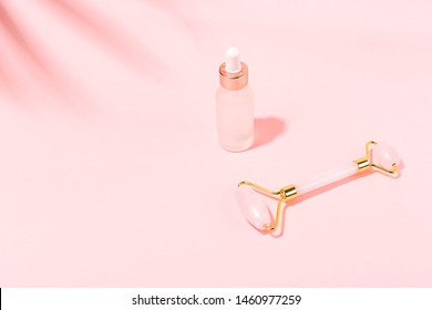 Creative shot of jade roller and serum bottle on pink background. Copy space.