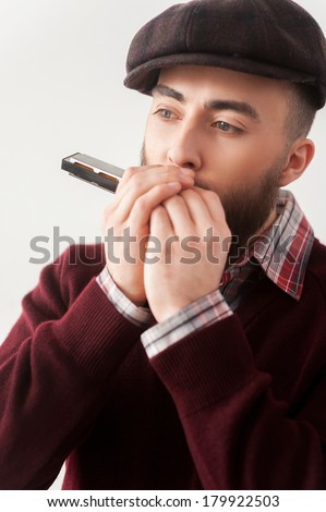 Creative soul.  Handsome young bearded men in hat playing harmonica