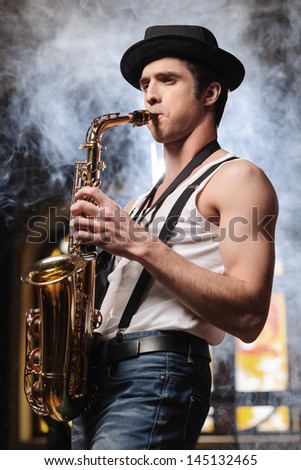 Creative soul.  Handsome young men in hat playing sax with a smoke on the background