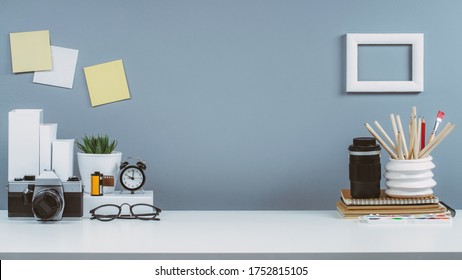 Creative space in art studio. Front view of the work desk with retro camera, office supplies and grey wall on the background. - Powered by Shutterstock