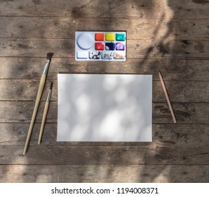 Creative space. Artistic work tools on dark wooden table watercolor, paintbrush and paper . Mock up. ,Creative space. ,Empty paper sheet with brushes and Watercolor
 over wooden table.