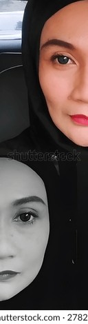 Creative split-screen vertical collage showing two halves of a beautiful Southeast Asian Muslim woman's face. 
The top image displays a close-up portrait in vibrant color with bold red lipstick, defined eyebrows, and grey contact lenses. 
The bottom image is a mirrored black and white portrait, creating a dramatic, artistic, and symmetrical duality concept. Perfect for beauty, makeup, hijab fashion, and conceptual art themes.