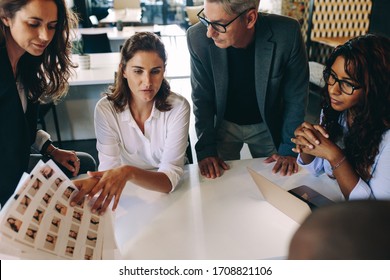 Creative Start-up Team Discussing Ideas In A Meeting. Group Of Multi Ethnic People During Business Meeting Looking At A Photo Contact Sheet.