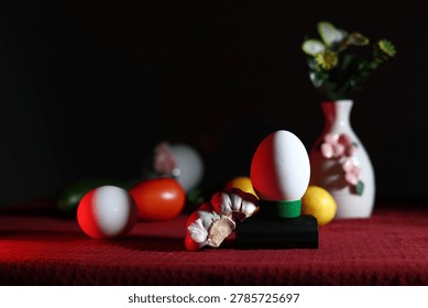 A creative still-life composition featuring white vases with flowers, eggs and fresh citrus fruits on a red surface with copy space. White eggs illuminated by beautiful blue and purple light refraction through a glass bottle on a dark background.