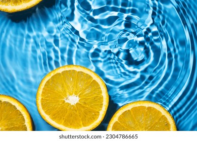 Creative summer background with orange fruit slices in swimming pool water. Summer wallpaper with copy space.