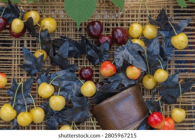 Creative summer composition featuring fresh yellow and red sweet cherries with decorative black leaves and rustic pottery in an artistic seasonal still life.