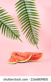Creative Summer fruit party concept of refreshing watermelons under a palm tree. Pastel pink background.