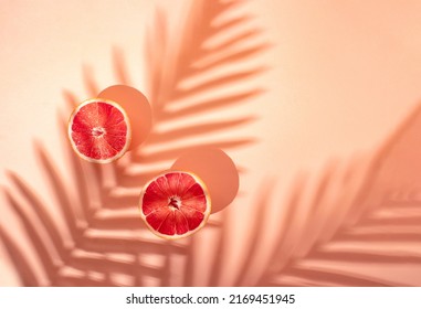 Creative Summer Fruit Party Concept Of Refreshing Grapefruit Under A Palm Tree. Pastel Pink Background.