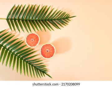 Creative Summer Fruit Party Concept Of Refreshing Grapefruit Under A Palm Tree. Pastel Pink Background.