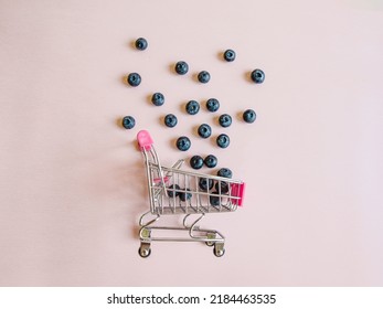 Creative Summer Layout Made Of Blueberries And Pink Shopping Cart Against Bright Pink Background. Original Blueberry Decoration. Minimal Summer Concept. Welcome Summer. Copy Space. 