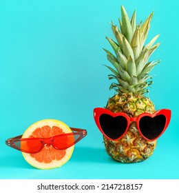 Creative summer layout made of pineapple with heart shaped red sunglasses and grapefruit with glasses against bright blue background. Original pineapple decoration. Minimal summer concept.