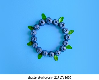 Creative Summer Round Frame Made Of Blueberries And Natural Green Leaves On Bright Blue Background. Original Blueberry Decoration. Minimal Summer Concept. Welcome Summer. Copy Space.