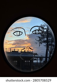 Creative sunset view through a round window with minimalist face illustration overlooking the ocean. Perfect for abstract art, travel, architecture, and coastal lifestyle concepts.