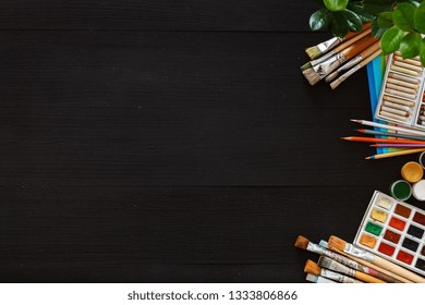 Creative supplies set on desk top view, tools for school creative work on black wooden table, blank background with drawing painting stationery shop, color paint brushes pencils, copy space, flat lay