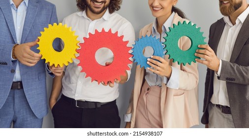 Creative Team Developing New Strategy And Building Effective Business System Together. Group Of Happy Young People Connecting Colorful Green, Blue, Red And Yellow Cogs. Teamwork And Synergy Concepts