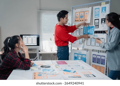 Creative team engaged in developing a mobile app interface, discussing design elements and user experience. Wireframes and prototypes displayed on the board and table