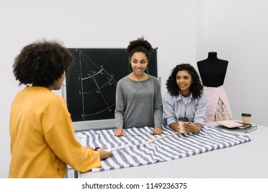 Creative team of smiling curly African American women planning new startup project in workplace. Brainstorming. University students learning fashion design at atelier. Young hipsters working together. - Powered by Shutterstock