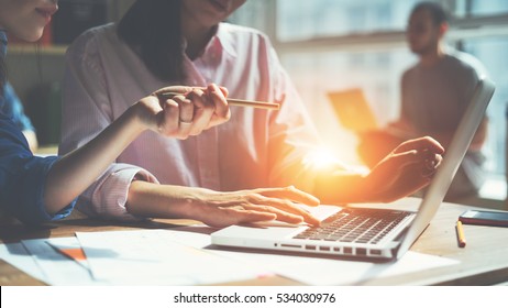 Creative Team Working On A Project In Loft Office. Two Women Discussing Marketing Plan. Laptop And Paperwork On The Table