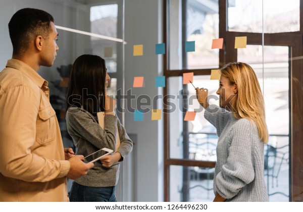 Creative team working together for startup\
project. Team building. Strategy planning. Brainstorming.\
Collaborate. Successful scrum master showing finger on sticky note,\
helping team reach\
consensus.